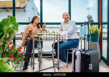 Un paio di viaggiatori che bevono caffè e che controllano qualcosa al telefono. Il bagaglio con maschere in primo piano. Portogallo. Foto Stock