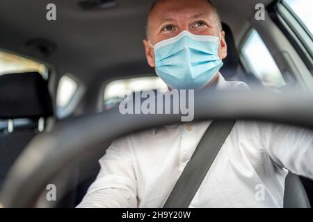 Un uomo in una maschera protettiva che guida un'auto, volante in primo piano, Portogallo Foto Stock