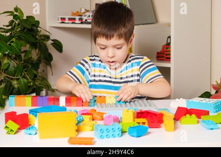 Un ragazzo di 4 anni in una T-shirt a righe gioca con mattoni multicolore del costruttore. Giochi educativi per bambini. Per un negozio di giocattoli Foto Stock