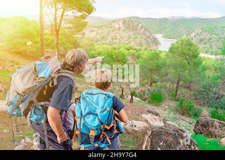 Il monitor Scout ragazzo nel mezzo della foresta indica e spiega a due escursionisti ragazzo la fine del percorso Foto Stock