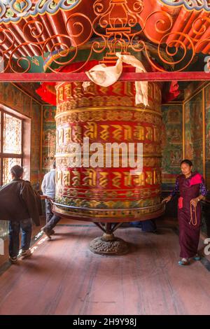 I fedeli girano una gigantesca ruota di preghiera nel monastero di Guru Lhakhang presso lo Stupa Boudhanath a Kathmandu, Nepal. Foto Stock