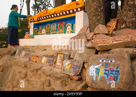 Una donna decora un santuario religioso con ghirlande di fiori nel complesso del tempio di Swayambhunath a Kathmandu, Nepal. Foto Stock