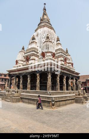 Un giovane ragazzo Newari rotola un vecchio pneumatico con un bastone nel borgo medievale di Bungamati, Nepal. Dietro c'è il Rato Machhendranath , un indù Foto Stock