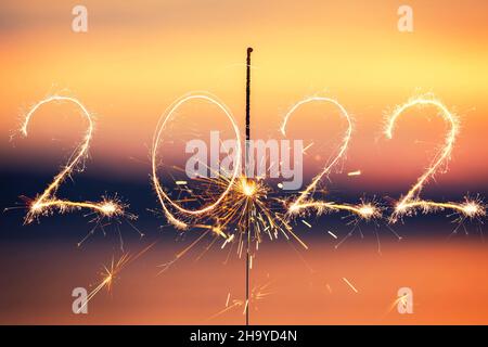 Felice anno nuovo 2022 testo scritto con scintille fuochi d'artificio su sfondo tramonto. Bengala fiamma. Foto Stock