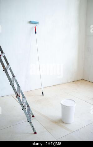 Scala a cavalletto, un secchio di plastica chiuso di vernice e un rullo di vernice, nella stanza. Preparazione per la riparazione. Foto Stock