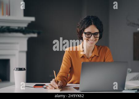 Piacevole felice giovane ragazza ispanica freelance che lavora su computer portatile a casa Foto Stock