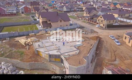 Vista dall'alto della base in cemento della casa. Clip. I lavoratori del cantiere controllano la base in calcestruzzo della casa in costruzione sullo sfondo del paese cottag Foto Stock