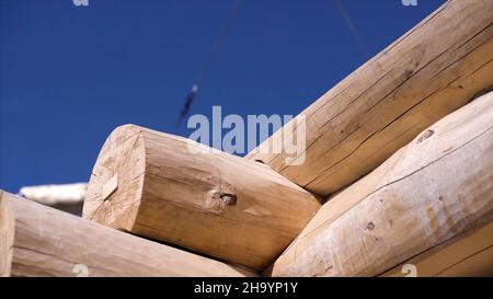 Primo piano di casa in legno e gru di sollevamento con legname. Clip. Casa in legno in costruzione su sfondo di gru con tronchi. Struttura in legno di hou Foto Stock