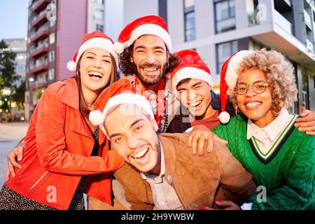 Selfie di un gruppo di amici che indossa il cappello di Babbo Natale. La gente festeggia il Natale all'aperto. Foto Stock