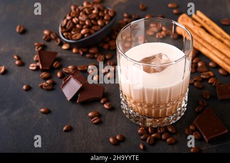 Bicchiere di crema irlandese liquore baileys con caffè torrefatto in chicchi, cannella e cioccolato su tavola di fondo in legno scuro. Messa a fuoco selettiva. Foto Stock