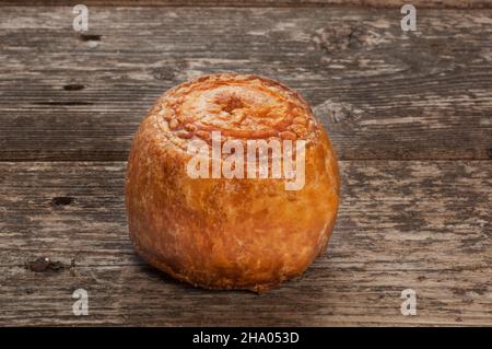 Studio di una piccola torta di maiale poggiata su un pannello di legno scuro - John Gollop Foto Stock