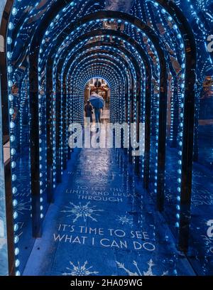 Una persona ripara sotto un ombrello in tunnel luce a Covent Garden, Londra, che è stato trasformato in blu per promuovere congelato. Foto Stock