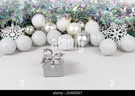 Scatole regalo argentate su sfondo sfocato con palline bianche e argentate, ghirlone e tinsel. Biglietto di Natale con palline bianche e argentate, ghirlanda Foto Stock