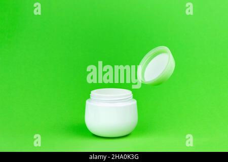 Vasetto per crema cosmetica con coperchio aperto su sfondo verde. Supplemento bottiglia vaso imballaggio Mockup Foto Stock