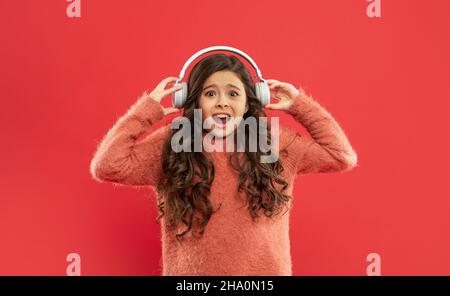 il bambino scioccato nel maglione ascolta musica ad alto volume in auricolari, musica Foto Stock