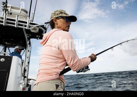 Una donna tiene la canna da pesca e guarda verso l'acqua sulla barca da pesca Foto Stock