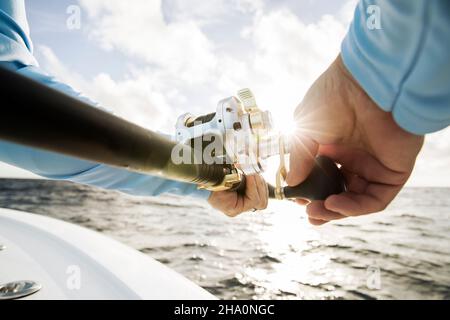 Primo piano di mans mani che si ribellano in canna da pesca con sunburst Foto Stock