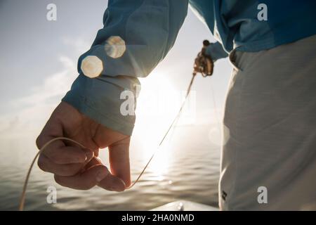 Un primo piano delle dita di mans che tengono la linea del volo con il sole che splende attraverso Foto Stock