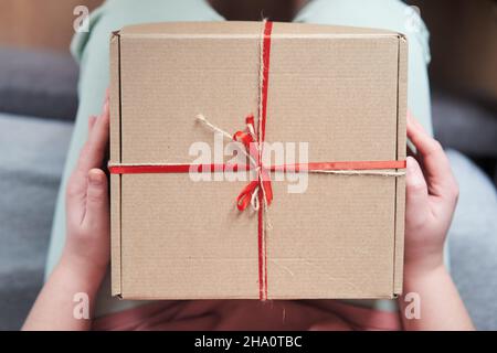 Messa a fuoco selezionata. Ragazza che tiene una scatola di regalo con un nastro rosso nelle sue mani Foto Stock