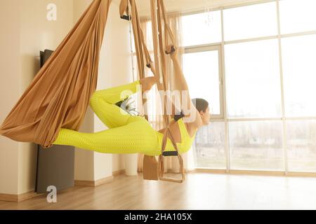 Ripresa posteriore di una donna che pratica yoga aereo, utilizzando amaca in studio, spazio copia Foto Stock