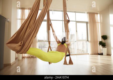 Scatto posteriore di vestibilità irriconoscibile donna forte che fa yoga aereo allo studio sportivo Foto Stock