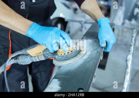 Levigare una parte della carrozzeria dell'auto con una smerigliatrice elettrica prima della verniciatura, servizio di riparazione carrozzeria del veicolo. Foto Stock