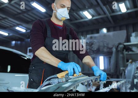 Levigare una parte della carrozzeria dell'auto con una smerigliatrice elettrica prima della verniciatura, servizio di riparazione carrozzeria del veicolo. Foto Stock