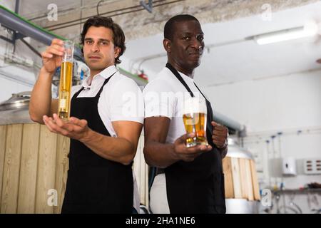 Due produttori di birra professionisti che mostrano il bicchiere e la bottiglia di birra Foto Stock