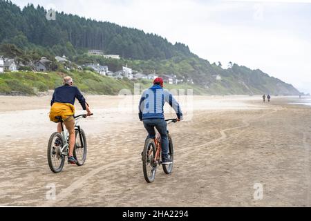 Due uomini dilettanti un padre anziano e un figlio giovane viaggiano fianco a fianco sulle biciclette di montagna lungo l'Oceano Pacifico nord-occidentale preferendo un lui attivo Foto Stock