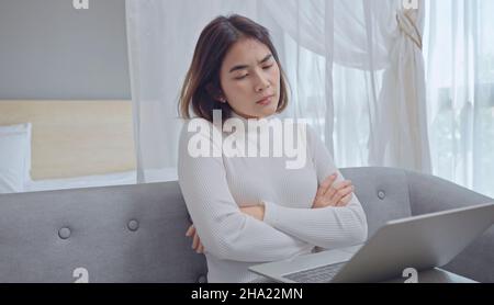 Stressata giovane donna che guarda lo schermo del computer portatile, che ha problemi con il progetto, seduta sul divano in soggiorno. Foto Stock