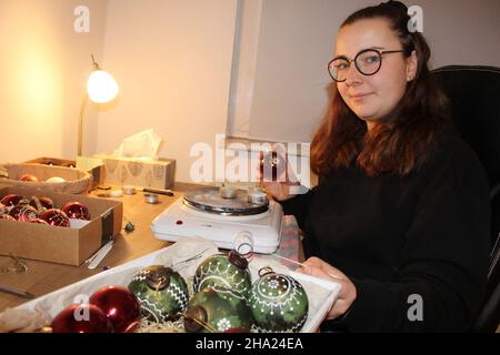 Burgneudorf, Germania. 30th Nov 2021. Annelie Rölke decora le palle dell'albero di Natale nel suo laboratorio di Natale. Normalmente, questi modelli originali Sorbian appartengono ai classici pasquali di Lusatia. Ma invece di uova, il 27-year-old abbra le palle dell'albero di Natale. (A dpa: 'Anziché le uova di Pasqua: Baubles di Natale Sorbian come decorazioni dell'albero') accreditamento: Miriam Schönbach/dpa-Zentralbild/dpa/Alamy Live News Foto Stock