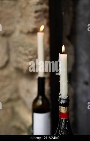 Le candele bruciano in bottiglie di vino e champagne sul davanzale. Vista frontale. Foto Stock