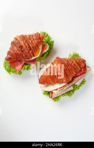 Due croissant con uova fritte, salmone salato, prosciutto, cetrioli freschi, pomodori e lattuga Foto Stock