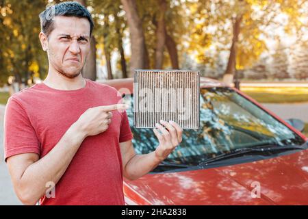 Conducente di auto frustrato con un'allergia alla polvere raccolta in un vecchio filtro di ventilazione sporco. Aria inquinata nella cabina Foto Stock