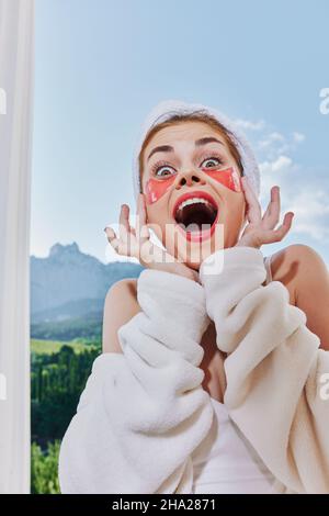 donna gioiosa con le toppe sul suo volto sullo sfondo della natura montagne sul balcone Foto Stock