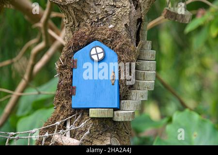 Primo piano di una porta fata con pochi passi ad essa, foglie verdi sullo sfondo. Un movimento artistico urbano di piccole porte fairy che colpiscono i cordoli, gli alberi e. Foto Stock