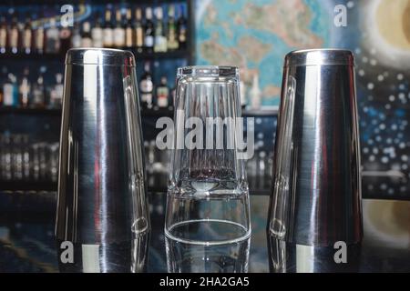 2 shaker di strumenti da bar per mescolare e preparare cocktail alcolici e bevande con un bicchiere sul banco bar. Foto Stock