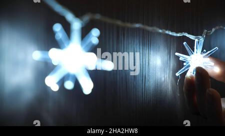 Primo piano della mano della donna che tocca la bellissima ghirlanda di Natale elettrica di luci luminose appese al guardaroba o alla porta di legno. Umore di Natale Foto Stock