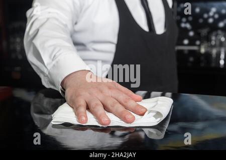 La mano di un barman professionale pulisce il bancone con un tovagliolo o un panno, pulisce e prepara il luogo di lavoro. Foto Stock