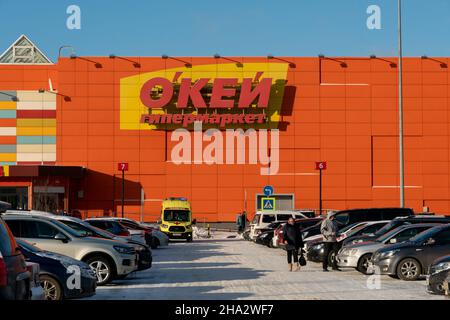 Auto e un'ambulanza stand di fronte all'ingresso del supermercato okay con il nome in russo sulla facciata in una giornata invernale soleggiata. Foto Stock