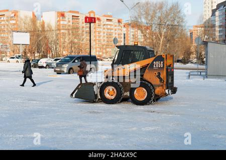 Una minipala caricatrice Mustang libera la neve all'esterno dopo una nevicata di fronte agli edifici residenziali in una giornata di sole. Foto Stock