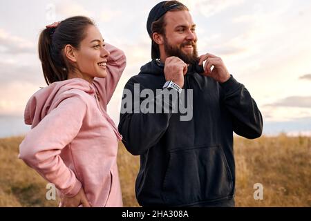 piacevole coppia trascorrere sano e attivo week-end in natura, preparandosi per il jogging. uomo caucasico e femmina hanno riposo, stare guardando di lato in contempla Foto Stock