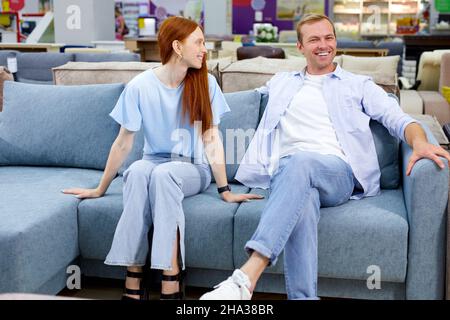 sorridente coppia è soddisfatto di scelta mobili moderni per la casa in negozio, sedersi insieme vogliono comprare, vestito casualmente. nel salone di mobili moderni, fare Foto Stock