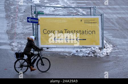 Monaco di Baviera, Germania. 10th Dic 2021. Una donna corre la bicicletta lungo il Theresienwiese, passando un poster con l'iscrizione 'Corona Teststation'. Credit: Sven Hoppe/dpa/Alamy Live News Foto Stock