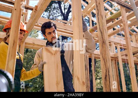 Imprese caucasiche lavoratori di carpentieri in zona di costruzione. Tema industriale. Edificio in legno con struttura a scheletro. Giovani uomini e donne in un lavoro Foto Stock