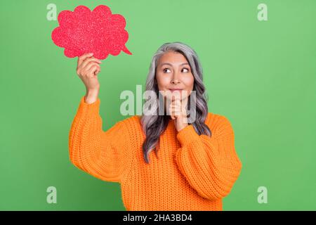 Foto di pensiero bianco hairdo invecchiato signora indossare arancione pullover isolato su sfondo verde Foto Stock