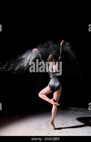 la splendida ballerina snella con ballerino, che indossa la tuta, che balla tra la nuvola di farina volante sullo sfondo nero dello studio, fa la performance. Conf Foto Stock