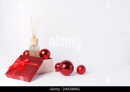 Profumo domestico di Natale o di Capodanno con i bastoni deodoranti dell'aria nella scatola del regalo rossa con le decorazioni su sfondo bianco. Aromaterapia vacanza invernale Foto Stock