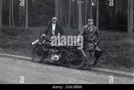 1930s, storico, un Signore e una signora, indossando cappotti e cappelli con il viso googles, in piedi per la loro moto, un indiano scout, con sidecar, su una pista di ghiaia accanto a una foresta, la Francia. L'iconico "Indian Scout" era una motocicletta costruita dal 1920 al 1949 e fu un luogo comune nel WW11 quando i 741, una versione appositamente realizzata, furono usati dai militari. Foto Stock