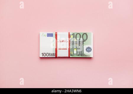 Pacchetto sigillato di banconote da 100 euro su sfondo rosa, concetto di minimalismo monetario vista dall'alto. Foto Stock